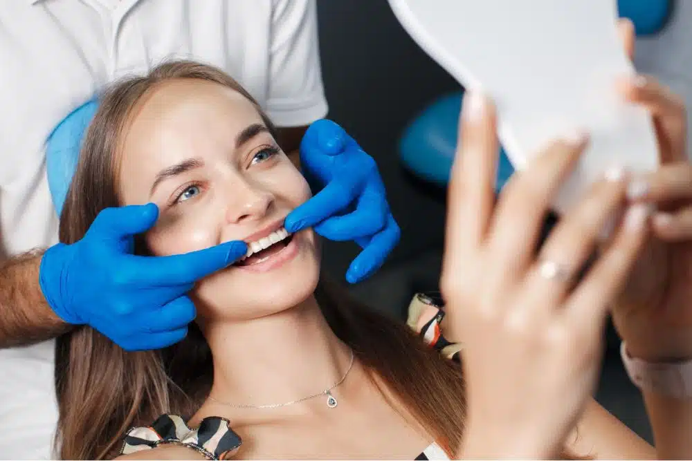 Gülümseyen hasta, diş hekiminin rehberliğinde şeffaf hizalayıcıların uyumunu kontrol ediyor